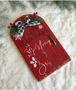 Detail of red wooden sleigh door sign with Merry & Bright text and faux greenery
