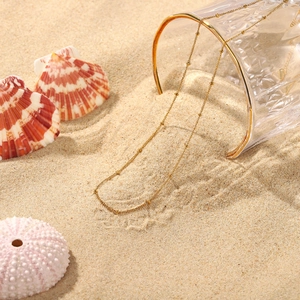 Collana a catena dorata con sfere in acciaio inox su sabbia tropicale con conchiglie marine