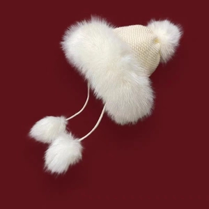 Detail of white knit winter hat featuring soft plush fur trim and hanging pom-poms