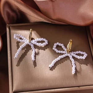 Detail of bow-shaped faux pearl earrings with golden rings on silk fabric texture