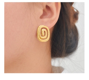 Gros plan de boucles d'oreilles spirales dorées texturées portées par un modèle