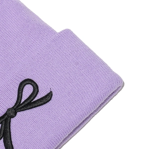 Détail d'un bonnet en tricot violet avec un écusson nœud noir et maille côtelée fine