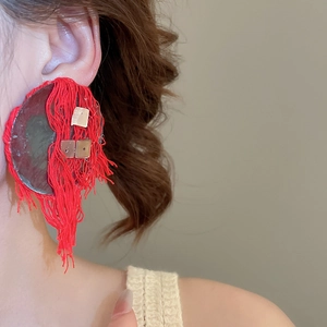 Close-up of red tassel earrings with gold square accents on a circular base
