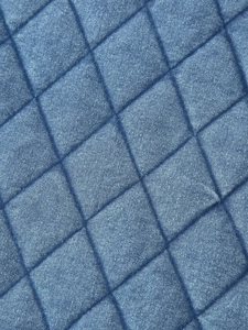 Detail shot of the blue quilted diamond pattern and washed denim fabric texture