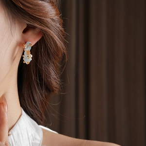 Macro detail of aquamarine flower earrings with C-shaped pearls on a model