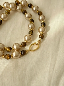 Detailed close-up of tiger eye stone pendant and champagne pearl necklace with gold clasp
