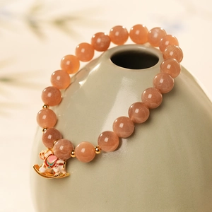Close-up of beaded sunstone bracelet with pink elephant charm on green vase
