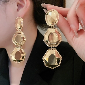 Gros plan de boucles d'oreilles pendantes géométriques dorées au fini métallique facetté