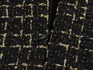 Dettaglio macro del tessuto tweed nero con fili dorati e cerniera invisibile premium