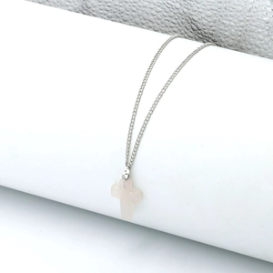 Detail of silver chain necklace with a pink quartz cross pendant on a white pedestal