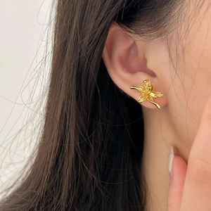Close-up of golden lily flower stud earrings on model ear in a minimalist style