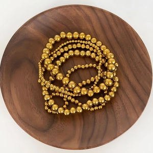 Dettaglio di bracciali a sfere placcati oro 18K su un vassoio in legno di noce