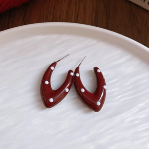 Detail of red acrylic C-shape earrings with white polka dots on a white ceramic plate