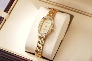 Gros plan d'une montre femme ovale dorée à quartz avec lunette en cristal dans un coffret