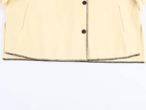 Detail of wool coat showing beige fabric with black blanket stitch and round buttons