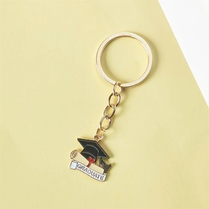 Gold metal graduation cap keychain with scroll pendant on flat lay background