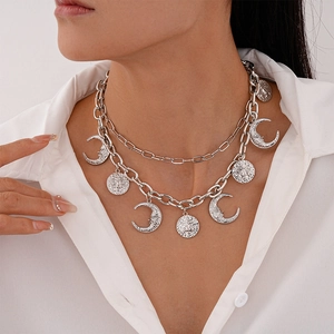 Detail of layered silver moon and sun pendant necklace worn on a white shirt