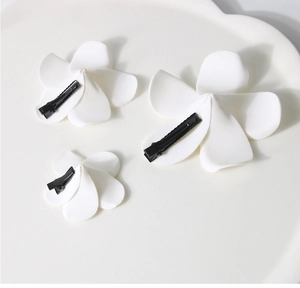 Detailed view of three white plumeria hair clips with black duckbill clips on a plate