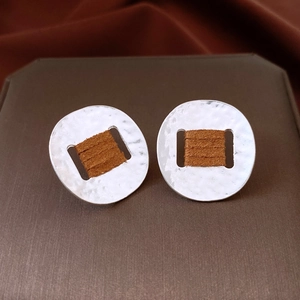 Detail of silver hammered metal earrings with brown suede wrap on jewelry display