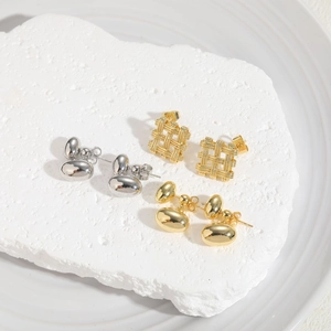 Detailed view of square braided and bean shaped metal earrings on a stone base