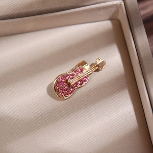 Gros plan d'une broche guitare dorée avec strass roses dans un écrin à bijoux beige