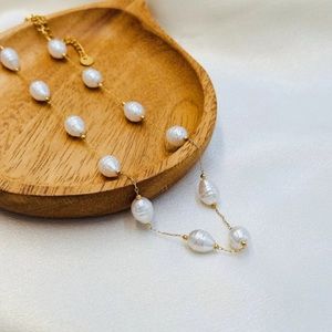 Elegant gold necklace with spaced baroque pearls over silk and wooden surface
