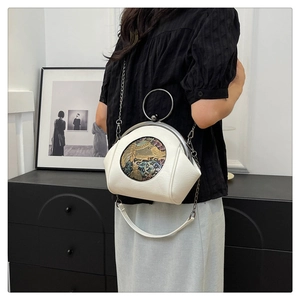 Close-up of white shell bag featuring detailed round embroidery and silver metal handle