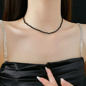 Detail view of a model wearing a minimalist black beaded crystal necklace on a dark background