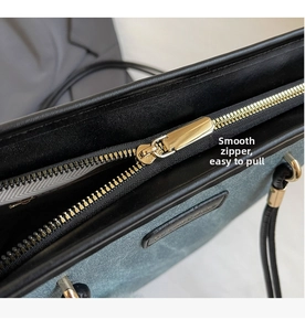 Detailed close-up of smooth golden metal zipper and logo patch on blue-gray tote bag