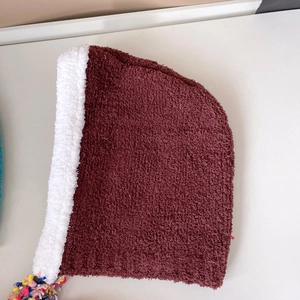 Detailed macro of burgundy plush winter hat with white faux fur lining and colorful tassels