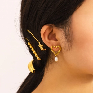 Golden heart earrings with freshwater pearl charms shown on a model with hair accessories