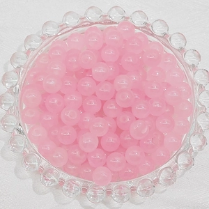 Detail of translucent pink glass beads in a textured glass bowl for DIY jewelry making