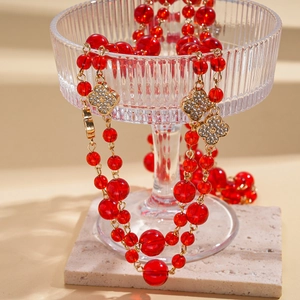 Close-up of red beaded necklace with crystal-studded golden clover pendant