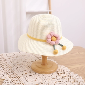 Détail d'un chapeau de paille crème avec un ruban jaune et une fleur rose tricotée