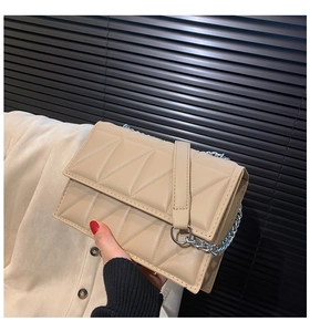 Detail of beige quilted shoulder bag with silver chain strap and metal hardware rings