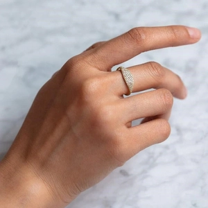 Close-up of a gold pavé diamond signet ring worn on index finger with marble background