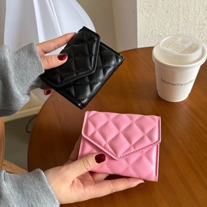 Quilted trifold wallets in black and pink PU leather held over a wooden table scene