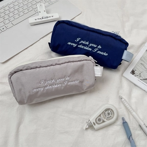 Navy blue and light grey pencil cases with embroidered quotes on a clean workspace