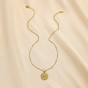 Detailed view of a gold zodiac pendant necklace with relief horse design on beige fabric