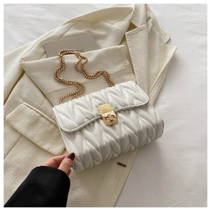 Detail of white quilted handbag with golden twist lock and elegant chain strap on a blazer