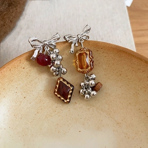 Macro shot of asymmetrical bow earrings with burgundy beads and amber gemstones on ceramic