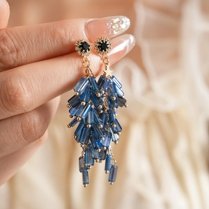 Detail of long gold earrings with blue beads and crystal-encrusted tassels