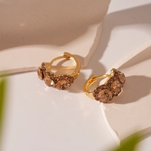 Elegant champagne crystal huggie earrings with gold base on a minimalist stone display