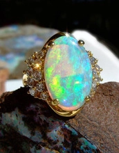 Macro shot of oval fire opal ring with brilliant green sparks and golden diamond halo