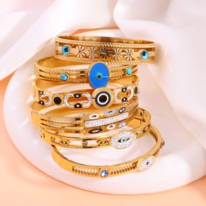 Detail of six gold-plated stainless steel evil eye bangles stacked on white tray
