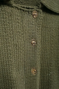 Dettaglio maglione in maglia verde militare con bottoni in metallo dorato a girello