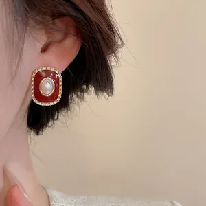 Detailed close-up of retro red pearl stud earrings with elegant gold gear borders
