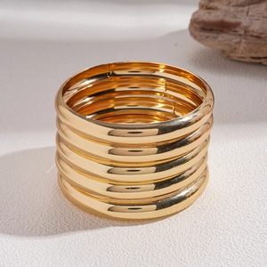 Detailed view of stackable gold-finished bangles on a textured surface with soft lighting