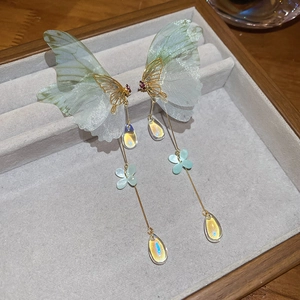 Detailed close-up of butterfly tassel earrings with green wings and golden pendants