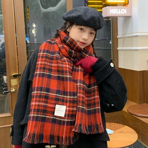 Detail of red plaid scarf with fringe and white woven label worn by a model in a cafe